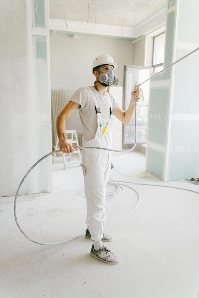 pexels photo 5493666 5493666 A construction worker in a white uniform using spray equipment inside a renovation site.